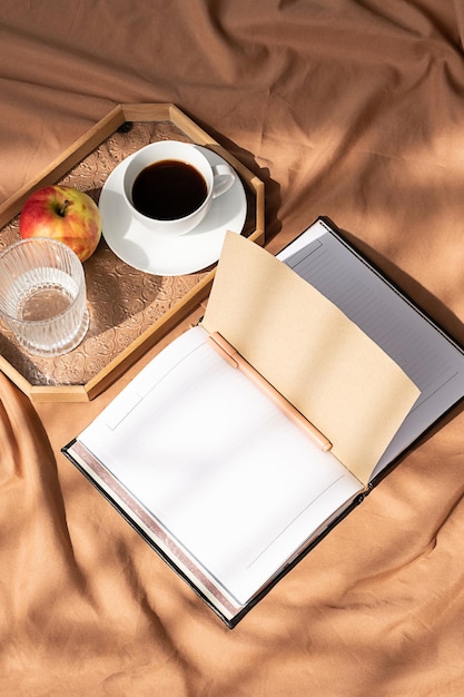 Öffnen Sie das Notizbuch und die Kaffeetasse auf dem Tablett, gemütlicher Morgen im Bett