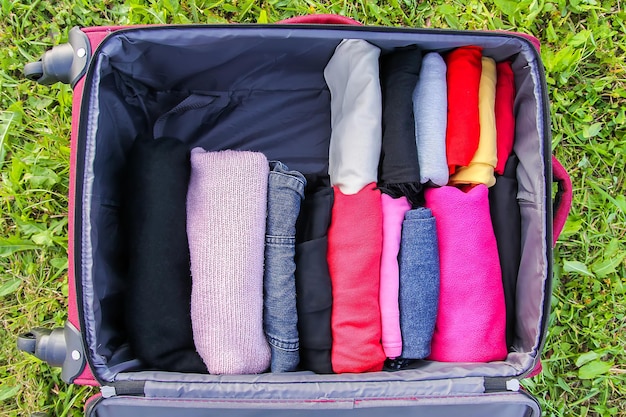 Öffnen Sie den Koffer auf dem grünen Gras mit verschiedenen vertikal gefalteten Kleidern. Vertikale Aufbewahrung für einfaches Reisen auf Reisen.