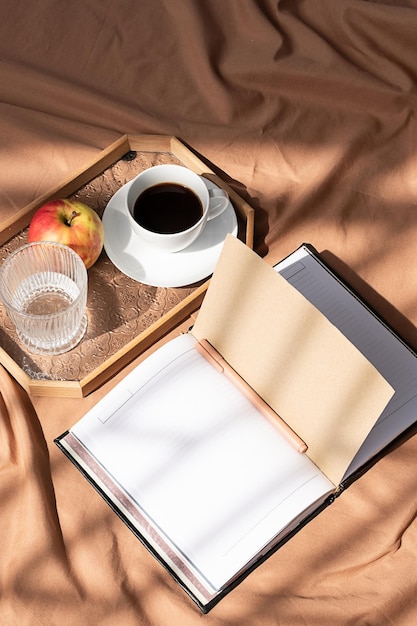 Öffnen Sie ein leeres Notizbuch und eine Kaffeetasse auf dem Bett Ein gemütlicher Morgen zu Hause