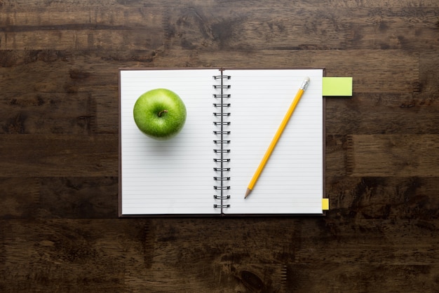 Öffnen Sie Notizbuch mit Apfel und Bleistift auf hölzerner Tabelle