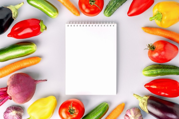 Öffnen Sie Notizbuch und frisches Gemüse auf grauem Hintergrund. Draufsicht. Einkaufsliste mit Gemüse.