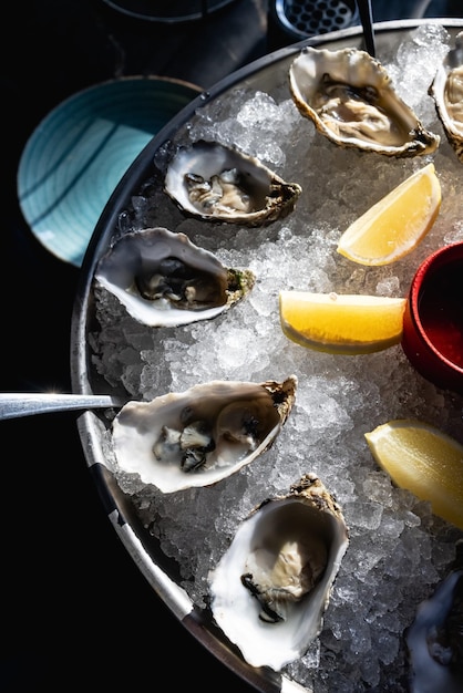 Öffnen Sie rohe Austern mit Zitrone und Rosmarin. Frische Meeresfrüchte auf einem Metalltablett über einem rustikalen Holz