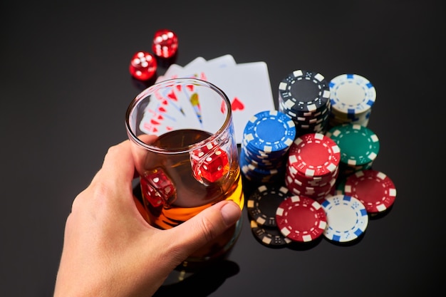 Fichas de casino jugando a las cartas vaso de whisky y dados sobre fondo reflectante oscuro