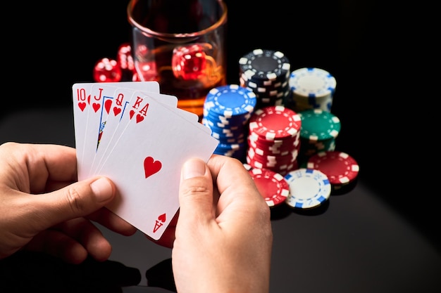 Fichas de casino jugando a las cartas vaso de whisky y dados sobre fondo reflectante oscuro