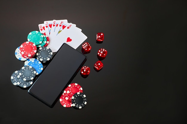 Fichas de cassino jogando dados de cartas e celular na mesa preta