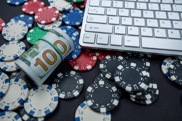 Fichas de pôquer e maços de dólares em um teclado de laptop espalhados sobre um fundo liso Jogos ilegais de jogos de pôquer