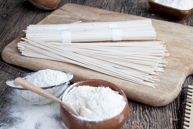 Fideos de arroz blanco y harina y otros ingredientes para cocinar fideos de arroz en un primer plano de la mesa de madera