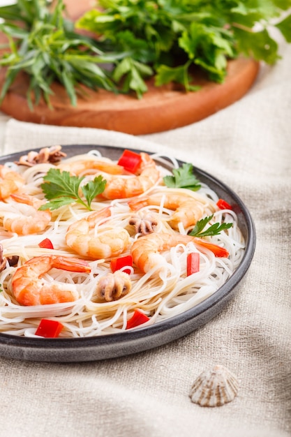 Fideos de arroz con camarones o langostinos y pequeños pulpos en placa de cerámica gris sobre un enfoque selectivo textil de lino blanco