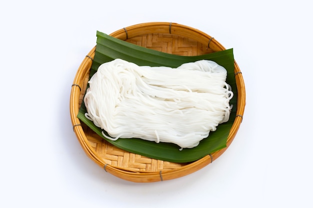 Fideos de arroz en cesta de bambú sobre fondo blanco.