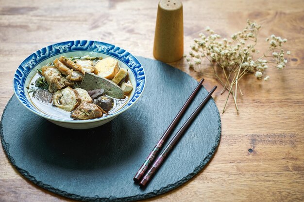 Foto fideos de arroz enrollados en caldo de cinco especias servido en una taza de azulejos sobre una mesa de madera