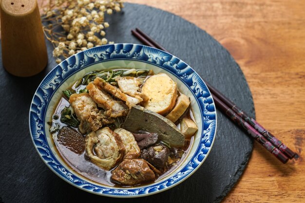 Foto fideos de arroz enrollados en caldo de cinco especias servido en una taza de azulejos sobre una mesa de madera