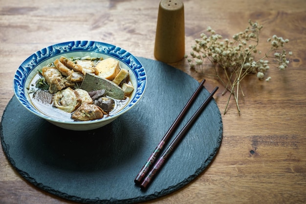 Foto fideos de arroz enrollados en caldo de cinco especias servido en una taza de azulejos sobre una mesa de madera