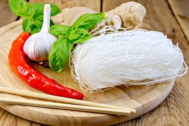 Fideos de arroz fino con ajo, pimiento rojo, jengibre, albahaca, palillos sobre un fondo de tablas de madera