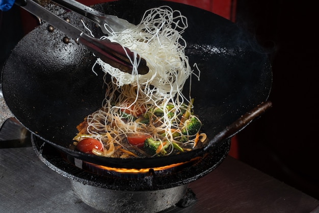 Foto fideos de arroz flambeados funchoza con verduras cocidas al fuego en sartén wok. comida de la calle.