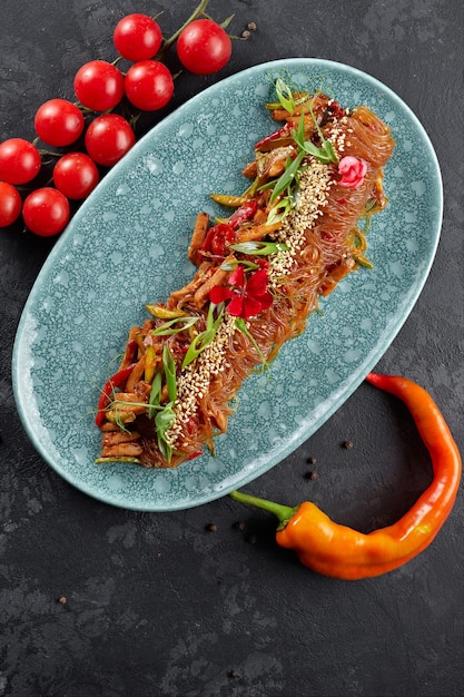 Fideos de arroz hervidos con verduras, semillas de sésamo, cebollas verdes, tomates cherry y pimiento rojo picante en un plato