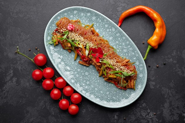 Fideos de arroz hervidos con verduras, semillas de sésamo, cebollas verdes, tomates cherry y pimiento rojo picante en un plato