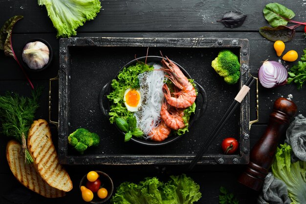 Fideos de arroz con huevo de gambas y verduras en un plato negro sobre un fondo de piedra negra Vista superior Espacio libre para el texto