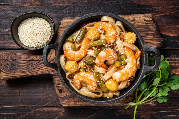 Fideos asiáticos salteados Udon con gambas gambas en una sartén. Fondo de madera oscura. Vista superior.