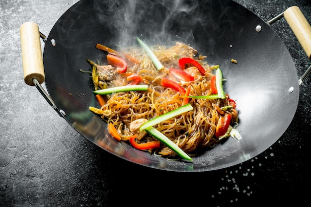 Foto fideos calientes de celofán en una sartén wok con pimientos, pepino y zanahorias