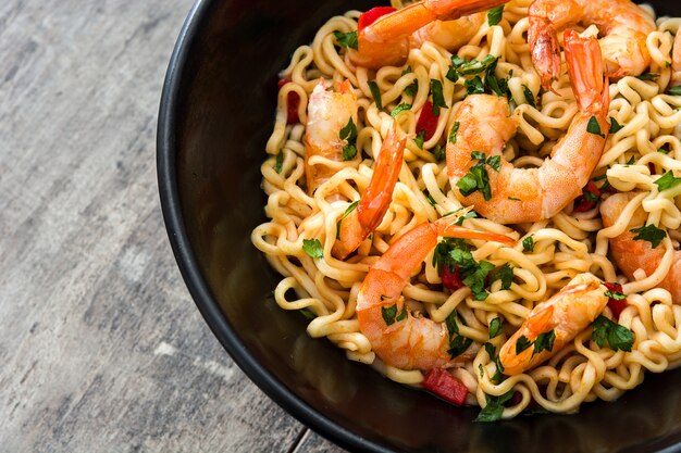 Fideos y camarones con verduras en un tazón negro sobre la mesa de madera de cerca