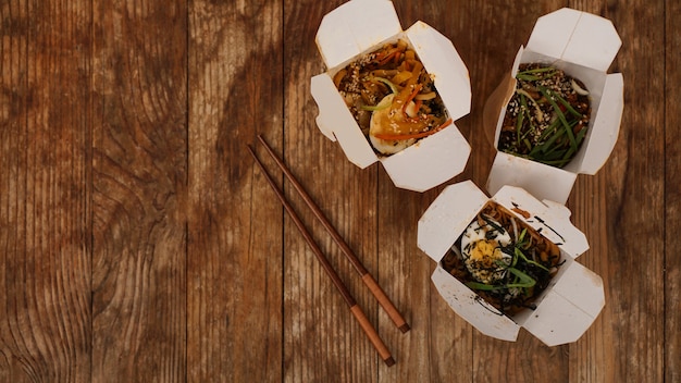 Fideos con carne de cerdo y verduras en caja para llevar sobre mesa de madera. Entrega de comida asiática. Alimentos en envases de papel sobre fondo de madera