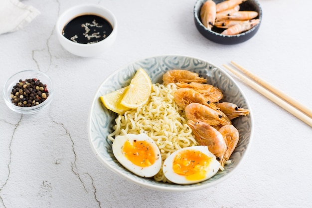 Fideos chinos con camarones fritos, huevo cocido y limón en un bol sobre la mesa Cocina asiática Primer plano