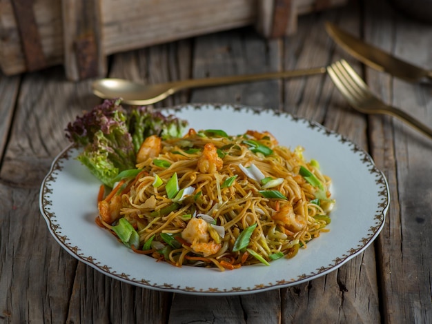 Fideos chinos con gambas servidos en un plato aislado en una vista lateral de fondo de madera de los fideos