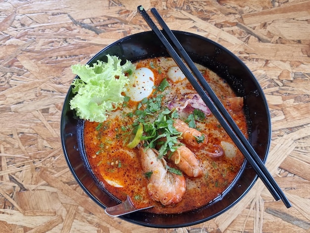 Fideos cremosos de Tom Yum en un tazón negro servido con albóndigas de calamar, gambas, lechuga y huevo cocido Primer plano centrado en el punto seleccionado