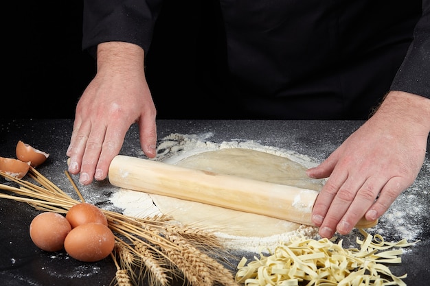 Fideos crudos caseros hechos de harina, huevo en un tazón de madera sobre negro