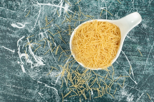 Foto fideos crudos en una cuchara, en el azul.