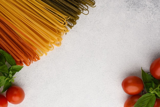 Fideos espaguetis vegetales con tomates cherry y marco de albahaca. Ingredientes de pasta sobre fondo de piedra blanca con espacio de copia.