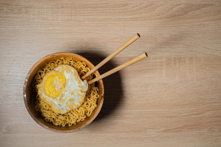 Fideos fritos y huevo SunnySide Up con palillos en un tazón de madera y una mesa de madera