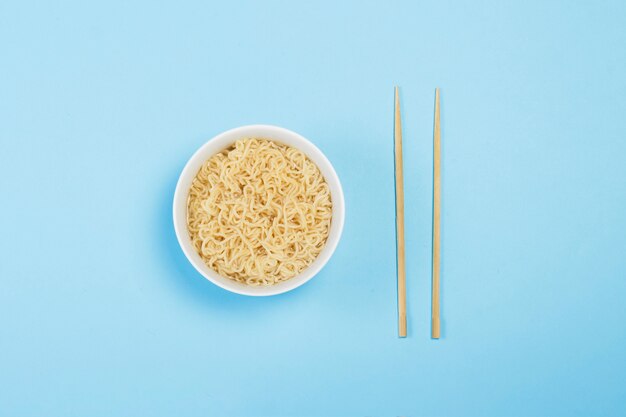 Fideos instantáneos asiáticos en un plato blanco y palos chinos sobre una superficie azul. El concepto de comida rápida, comida rápida, comida chatarra. Vista plana, vista superior.