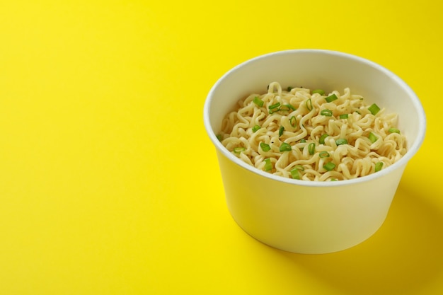 Fideos instantáneos cocidos en vaso de papel sobre amarillo