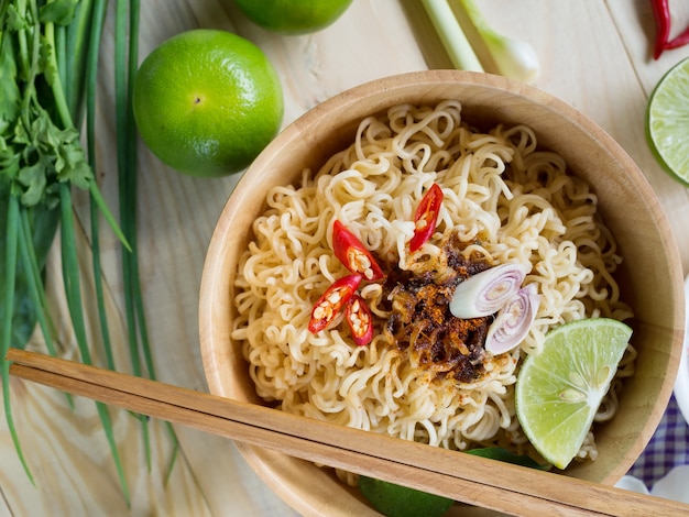 Fideos instantáneos en cuenco de madera y guarniciones de verduras en la mesa de madera. vista superior