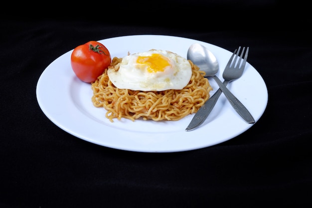 Fideos instantáneos fritos con huevo y tomate en un plato, sobre un fondo negro