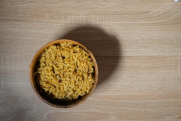 Fideos instantáneos fritos en un tazón de madera y una mesa de madera