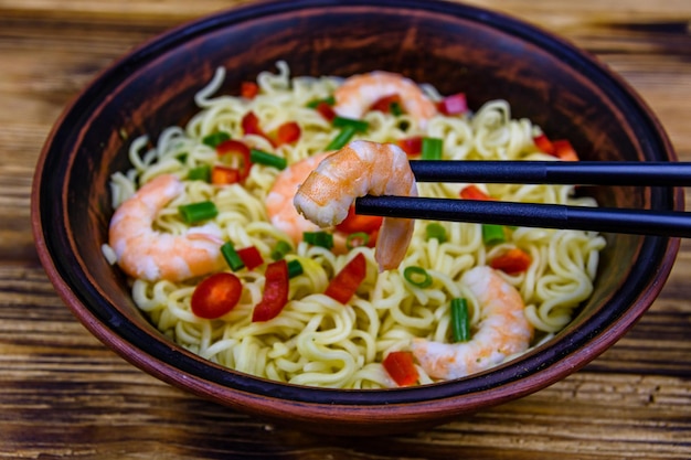 Fideos instantáneos con gambas, pimiento rojo y cebolla verde en un cuenco de cerámica. Comida japonesa. Palillos con camarones