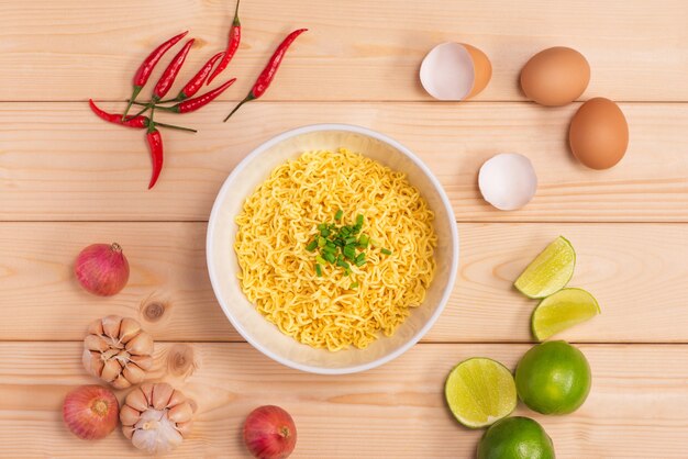 Fideos instantáneos en un recipiente con verduras sobre fondo de madera