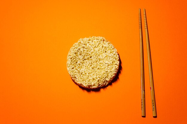 Fideos instantáneos secos y palillos en el fondo naranja