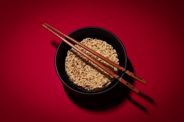 Fideos instantáneos secos y palillos en el fondo rojo.