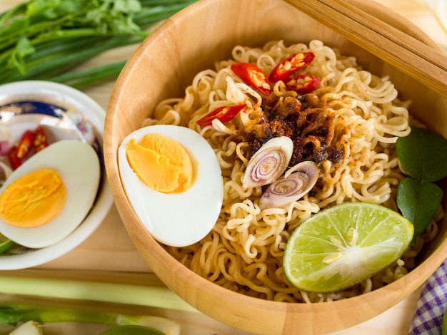 Fideos instantáneos en tazón de madera y guarniciones de verduras sobre fondo de mesa de madera