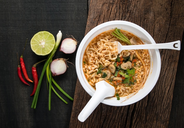 Fideos instantáneos en tazón de plástico y guarniciones de verduras en madera