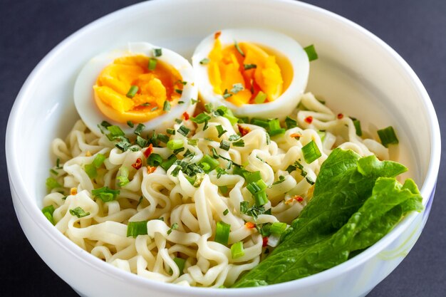 Fideos instantáneos con verduras y huevo en un plato. Tazón de fideos en blanco