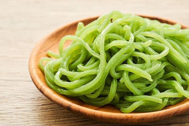 fideos konjac verdes en placa de madera sobre fondo de mesa de madera