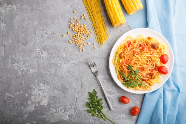 Fideos de maíz con salsa de tomate y rúcula sobre un fondo de hormigón gris. Vista superior, copia espacio.