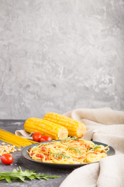 Fideos de maíz con salsa de tomate y rúcula sobre una superficie de hormigón negro. Vista lateral, copia espacio.