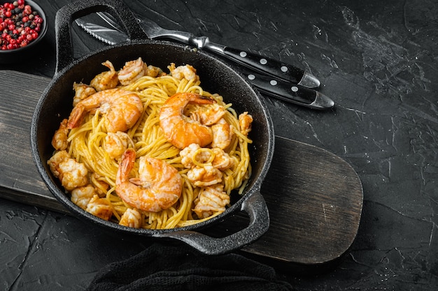 Fideos con mariscos, en sartén de hierro fundido, sobre fondo de piedra negra, con espacio para copiar texto