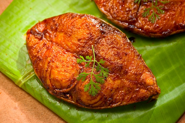 Fideos de pescado vidente dispuestos maravillosamente y adornados con hojas de cilantro sobre una base cubierta de hojas de plátano que se coloca sobre un fondo texturizado de madera