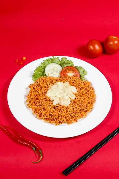 Fideos picantes con cobertura y verduras sobre fondo rojo.